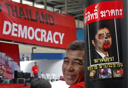 An anti-government "red shirt" protester sits next to a defaced portrait of Thailand's Prime Minister Abhisit Vejjajiva in the main shopping district in Bangkok April 18, 2010. REUTERS/Eric Gaillard
An anti-government "red shirt" protester sits next to a defaced portrait of Thailand's Prime Minister Abhisit Vejjajiva in the main shopping district in Bangkok April 18, 2010. REUTERS/Eric Gaillard