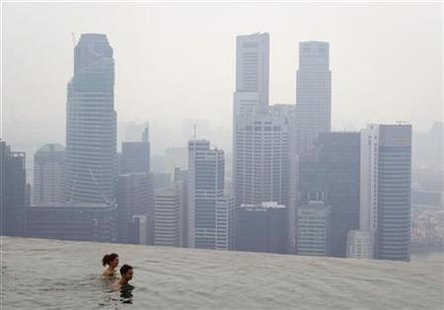 
Hotel guests swim in an infinity pool overlooking the haze-covered skyline in Singapore October 22, 2010. REUTERS/Vivek Prakash
