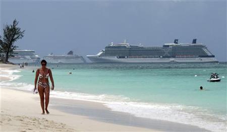 
A woman walks along Seven Mile Beach with three cruise ships anchored in port in George Town, Cayman Islands, April 27, 2010. REUTERS/Gary Hershorn
