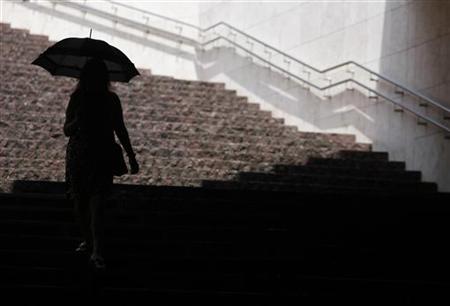 A woman using an umbrella to shield herself from the sun as she walks down stairs at a business complex in Tokyo A woman using an umbrella to shield herself from the sun as she walks down stairs at a business complex in Tokyo