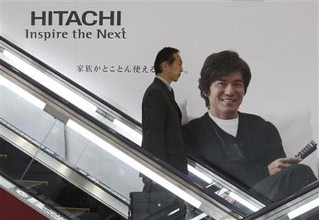 A man coming down an escalator passes an advertisement for Hitachi in Tokyo
