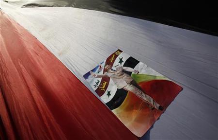 A poster depicting Syria's President Bashar al-Assad is seen on a giant Syrian flag carried by Syrian supporters living in Lebanon in front A poster depicting Syria's President Bashar al-Assad is seen on a giant Syrian flag carried by Syrian supporters living in Lebanon in front