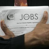 Man carrying a stack of job listings listens to a discussion at the One Stop employment center in San Francisco