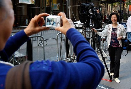 A tourist poses for a picture next to a television camera as media gather outside of the building where Dominique Strauss-Kahn is currently 