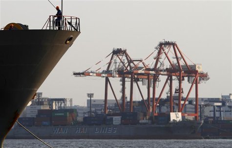 A worker stands on a ship in front of a cargo ship at a port in Tokyo