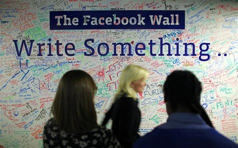 People walk past the Facebook wall inside their office in New York People walk past the Facebook wall inside their office in New York