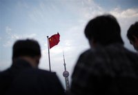 People stand near a Chinese flag as the Oriental Pearl TV tower is seen in the financial area of Pudong in Shanghai
