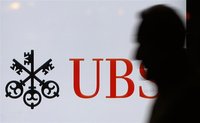 A man passes a UBS logo displayed on a screen in a window of a UBS bank building in Bern