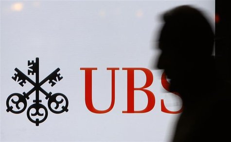 A man passes a UBS logo displayed on a screen in a window of a UBS bank building in Bern
