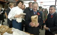 An aide (R) digs money out of his pocket for Britain's Prince Charles (C) to purchase a five dollar loaf of artisans bread, at traditional farmer's market, at the Evergreen Brick Works Restoration site, in Toronto November 6, 2009. Prince Charles and wife Camilla the Duchess of Cornwall are currently on an 11 day tour of Canada. REUTERS/Fred Thornhill (CANADA POLITICS ROYALS)