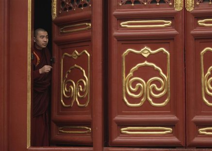 A Buddhist monk looks from behind a door before worship during the Tibetan New Year celebrations at Yonghegong Lama Temple in Beijing