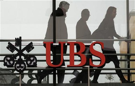 People walk behind the logo of Swiss bank UBS in Zurich