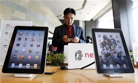 Customer holds Apple Inc iPhone 4 smartphone on display behind company's iPad tablets at headquarters of South Korean mobile carrier KT in S Customer holds Apple Inc iPhone 4 smartphone on display behind company's iPad tablets at headquarters of South Korean mobile carrier KT in S