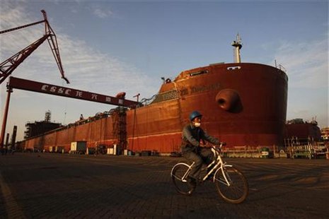 An employee rides a bicycle past a nearly completed ship at China State Shipbuilding Corporation (CSSC) Longxue shipbuilding, in the souther An employee rides a bicycle past a nearly completed ship at China State Shipbuilding Corporation (CSSC) Longxue shipbuilding, in the souther