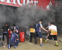 Williams Formula One team crew members try to extinguish, with the help of other teams' crew, a fire that broke out inside their garage foll