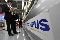 A man is seen next to an Olympus logo at an electronics shop in Tokyo May 10, 2012. REUTERS/Kim Kyung-Hoon