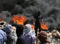 Lebanese Sunni Muslim men, with faces covered, stand, after they burnt tyres to block a road to protest the killing of Sheikh Ahmed Abdul Wa