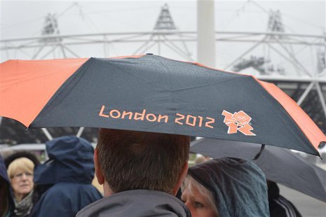 A spectator shelters under an umbrella with a London 2012 Olympics logo in the Olympic Park at Stratford, east London May 3, 2012. REUTERS/T A spectator shelters under an umbrella with a London 2012 Olympics logo in the Olympic Park at Stratford, east London May 3, 2012. REUTERS/T