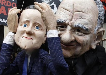 A demonstrator dressed as Rupert Murdoch holds a puppet depicting Britain's Prime Minister David Cameron as he protests outside the High Cou A demonstrator dressed as Rupert Murdoch holds a puppet depicting Britain's Prime Minister David Cameron as he protests outside the High Cou