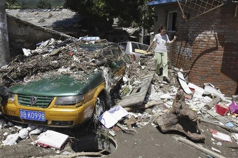 A resident walks past debris and a taxi damaged by a flood after heavy rainfalls hit Mentougou District in Beijing July 22, 2012. REUTERS/St A resident walks past debris and a taxi damaged by a flood after heavy rainfalls hit Mentougou District in Beijing July 22, 2012. REUTERS/St