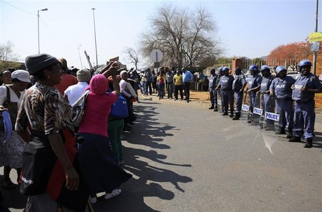 Police keep watch as women sing before the arrival of some of the 250 mine workers who were arrested last Thursday when they had a shoot out Police keep watch as women sing before the arrival of some of the 250 mine workers who were arrested last Thursday when they had a shoot out