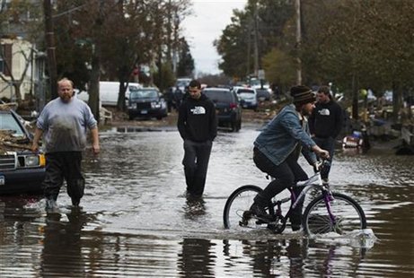 A man rides a bike past three others walking through water still sitting in the streets to survey damage from Hurricane Sandy in the New Dor A man rides a bike past three others walking through water still sitting in the streets to survey damage from Hurricane Sandy in the New Dor