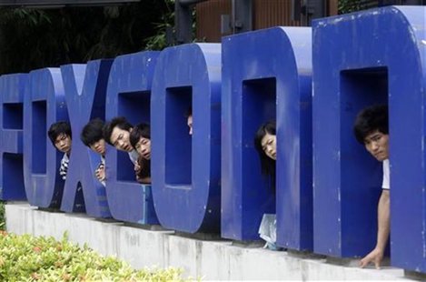 Workers look on from a Foxconn logo near the gate of a Foxconn factory in the township of Longhua, Guangdong province May 29, 2010. REUTERS/ Workers look on from a Foxconn logo near the gate of a Foxconn factory in the township of Longhua, Guangdong province May 29, 2010. REUTERS/