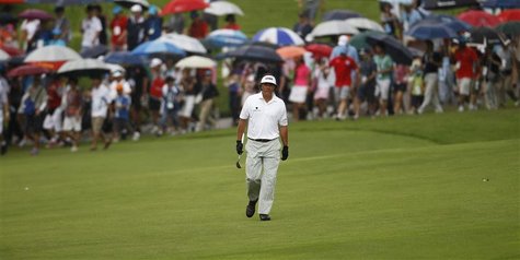 Phil Mickelson of the U.S. walks down the eighth fairway as spectators carrying umbrellas follow in the light drizzle during the rain-delaye Phil Mickelson of the U.S. walks down the eighth fairway as spectators carrying umbrellas follow in the light drizzle during the rain-delaye