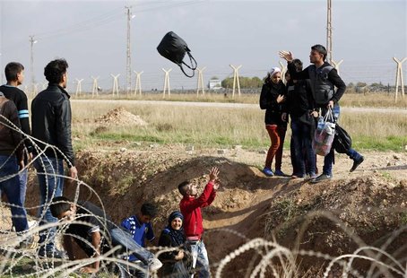 Syrians throw their belongings while trying to cross a ditch after crossing from the northern Syrian town of Ras al-Ain to Turkey in the bor Syrians throw their belongings while trying to cross a ditch after crossing from the northern Syrian town of Ras al-Ain to Turkey in the bor