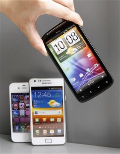 A shop attendant poses with replicas of HTC, Samsung and Apple's smartphones inside a mobile phone shop in Taipei April 6, 2012. REUTERS/She A shop attendant poses with replicas of HTC, Samsung and Apple's smartphones inside a mobile phone shop in Taipei April 6, 2012. REUTERS/She
