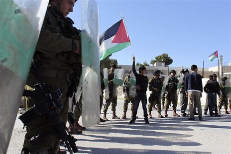 A Palestinian youth (C) waves a flag in front of Israeli soldiers during a demonstration in the West Bank village of al-Masara near Bethlehe A Palestinian youth (C) waves a flag in front of Israeli soldiers during a demonstration in the West Bank village of al-Masara near Bethlehe