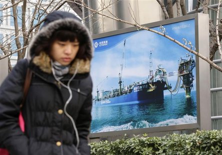 A woman walks past a poster showing an offshore work platform from the China National Offshore Oil Corp (CNOOC) next to its headquarters bui A woman walks past a poster showing an offshore work platform from the China National Offshore Oil Corp (CNOOC) next to its headquarters bui