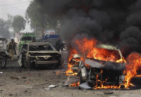 A police officer and a citizen walk towards a burning car after a bomb attack, at Fauji Market in Peshawar December 17, 2012. REUTERS/Ameerz A police officer and a citizen walk towards a burning car after a bomb attack, at Fauji Market in Peshawar December 17, 2012. REUTERS/Ameerz