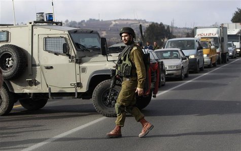 An Israeli soldier walks in front of a military vehicle blocking traffic on a road near the scene of a shooting in al-Arroub refugee camp ne An Israeli soldier walks in front of a military vehicle blocking traffic on a road near the scene of a shooting in al-Arroub refugee camp ne