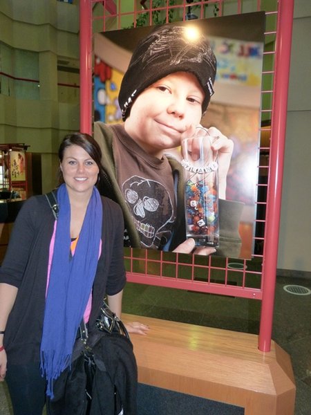 Jess Kelley in front of the picture of the young boy holding his legacy beads. These beads represent a procedure, therapy or medication the child has completed in treatment - the picture speaks for itself - that little guy has been through a lot.