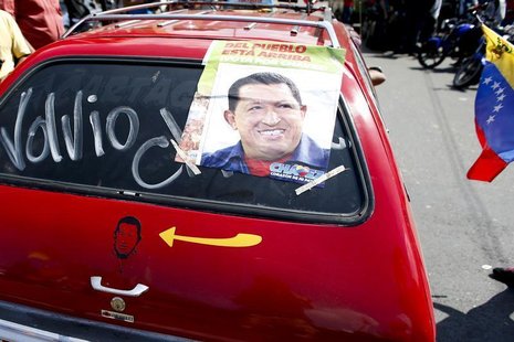 A car with a picture and poster of Venezuela's President Hugo Chavez and the word "he's back' drives past a military hospital, where Chavez A car with a picture and poster of Venezuela's President Hugo Chavez and the word "he's back' drives past a military hospital, where Chavez