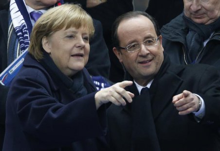 France's President Francois Hollande (R) points with German Chancellor Angela Merkel as they attend an international friendly soccer match b France's President Francois Hollande (R) points with German Chancellor Angela Merkel as they attend an international friendly soccer match b