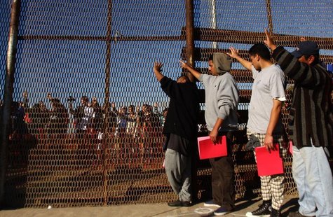 A group of recently deported immigrants stand near the double steel fence that separates San Diego and Tijuana at the border in Tijuana Dece A group of recently deported immigrants stand near the double steel fence that separates San Diego and Tijuana at the border in Tijuana Dece