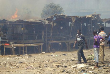 Men stand and watch as a fire rages in the background during clashes between rival gangs in Marche Madina, in Conakry March 1, 2013. REUTERS Men stand and watch as a fire rages in the background during clashes between rival gangs in Marche Madina, in Conakry March 1, 2013. REUTERS