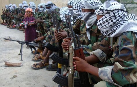 A boy carrying a toy gun stands near members of Somalia's hardline al Shabaab rebel group after attending Eid al-Adha prayers inside a footb A boy carrying a toy gun stands near members of Somalia's hardline al Shabaab rebel group after attending Eid al-Adha prayers inside a footb