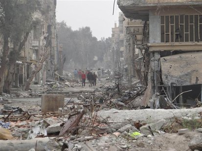 People walk on a street lined with buildings damaged by what activists said were missiles fired by a Syrian Air Force fighter jet loyal to P People walk on a street lined with buildings damaged by what activists said were missiles fired by a Syrian Air Force fighter jet loyal to P