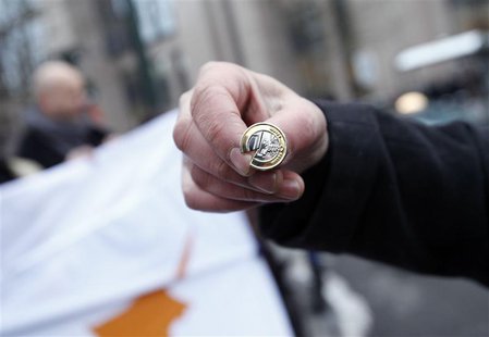 A man holds a broken 1-euro coin pin during a protest comprising of around 40 people from Cyprus, outside a Eurogroup meeting at the Europea A man holds a broken 1-euro coin pin during a protest comprising of around 40 people from Cyprus, outside a Eurogroup meeting at the Europea