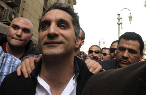 Bassem Youssef (C), the country's best-known satirist, gestures to journalists and activists as he arrives at the high court to appear at th Bassem Youssef (C), the country's best-known satirist, gestures to journalists and activists as he arrives at the high court to appear at th