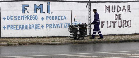A city cleaner works near a wall with graffiti that reads "International Monetary Fund + Unemployment + Poverty + Precariousness + Privatiza A city cleaner works near a wall with graffiti that reads "International Monetary Fund + Unemployment + Poverty + Precariousness + Privatiza