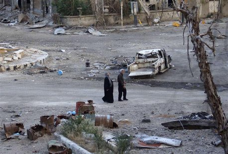 People walk past a destroyed car in a street lined with damaged buildings in Deir al-Zor April 15, 2013. Picture taken April 15, 2013. REUTE People walk past a destroyed car in a street lined with damaged buildings in Deir al-Zor April 15, 2013. Picture taken April 15, 2013. REUTE