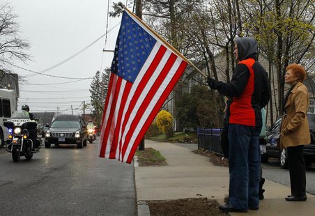 Richard Corapi holds a U.S. flag from a sidewalk while the hearse carrying the body of Massachusetts Institute of Technology (MIT) police of Richard Corapi holds a U.S. flag from a sidewalk while the hearse carrying the body of Massachusetts Institute of Technology (MIT) police of