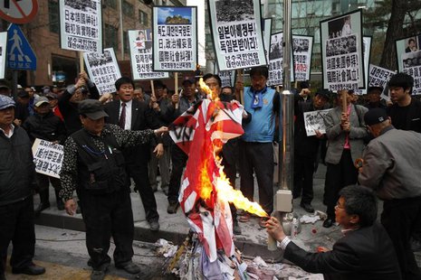 A South Korean conservative right-wing protester burns a Japanese "rising sun" flag as they chant slogans during an anti-Japan rally in fron A South Korean conservative right-wing protester burns a Japanese "rising sun" flag as they chant slogans during an anti-Japan rally in fron