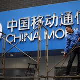A labourer works in front of a sign for China Mobile at the company's office in downtown Shanghai March 11, 2013. REUTERS/Carlos Barria