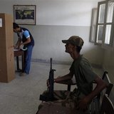 An army soldier (R) sits on a chair while a voter stamps his ballot papers inside a booth at a polling station during a re-polling for the g An army soldier (R) sits on a chair while a voter stamps his ballot papers inside a booth at a polling station during a re-polling for the g