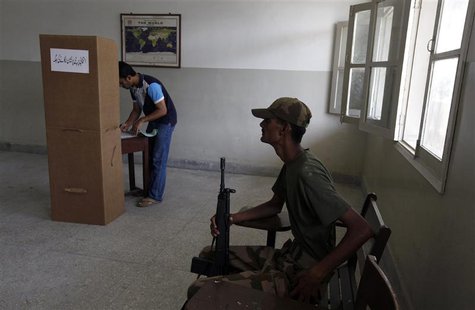 An army soldier (R) sits on a chair while a voter stamps his ballot papers inside a booth at a polling station during a re-polling for the g An army soldier (R) sits on a chair while a voter stamps his ballot papers inside a booth at a polling station during a re-polling for the g